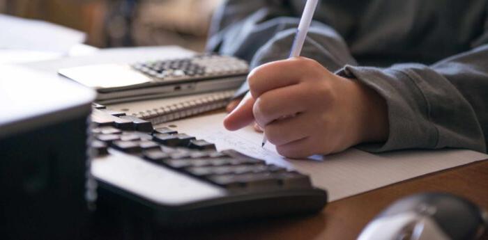 An individual completing a problem on paper in front of a computer.