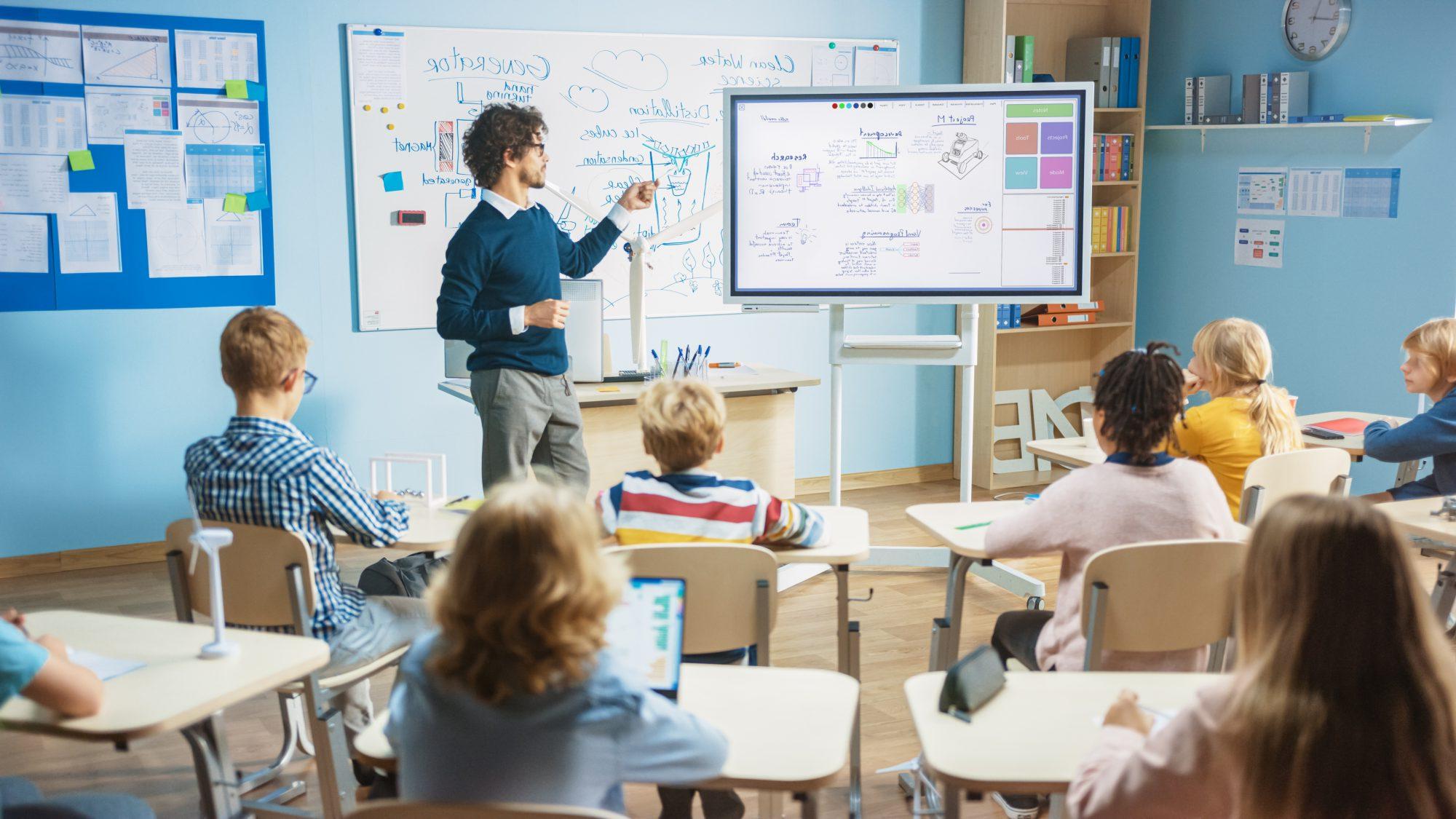 一名男子指着小学生课桌前的一块白板