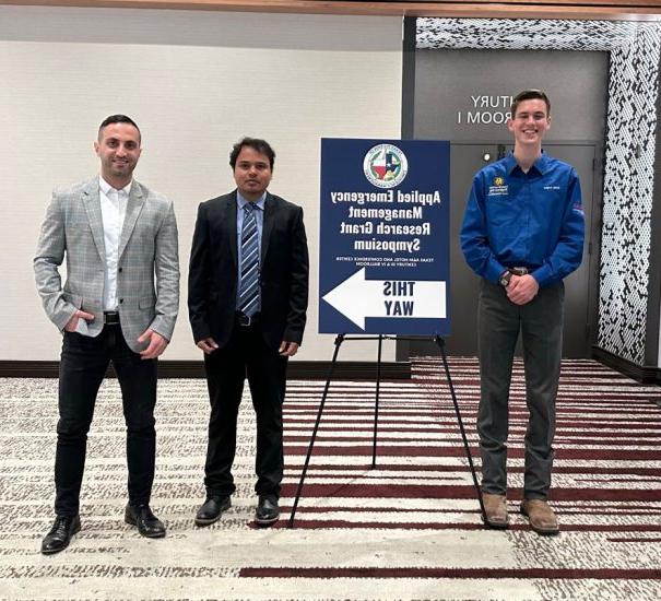 Three researchers stand next to a poster directing attendees.